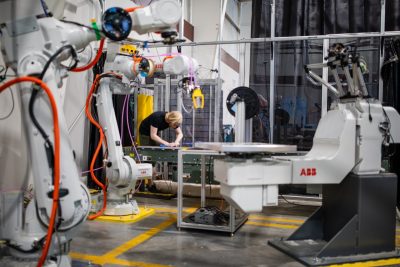 A graduate student works near several large white robotic arms in a laboratory.